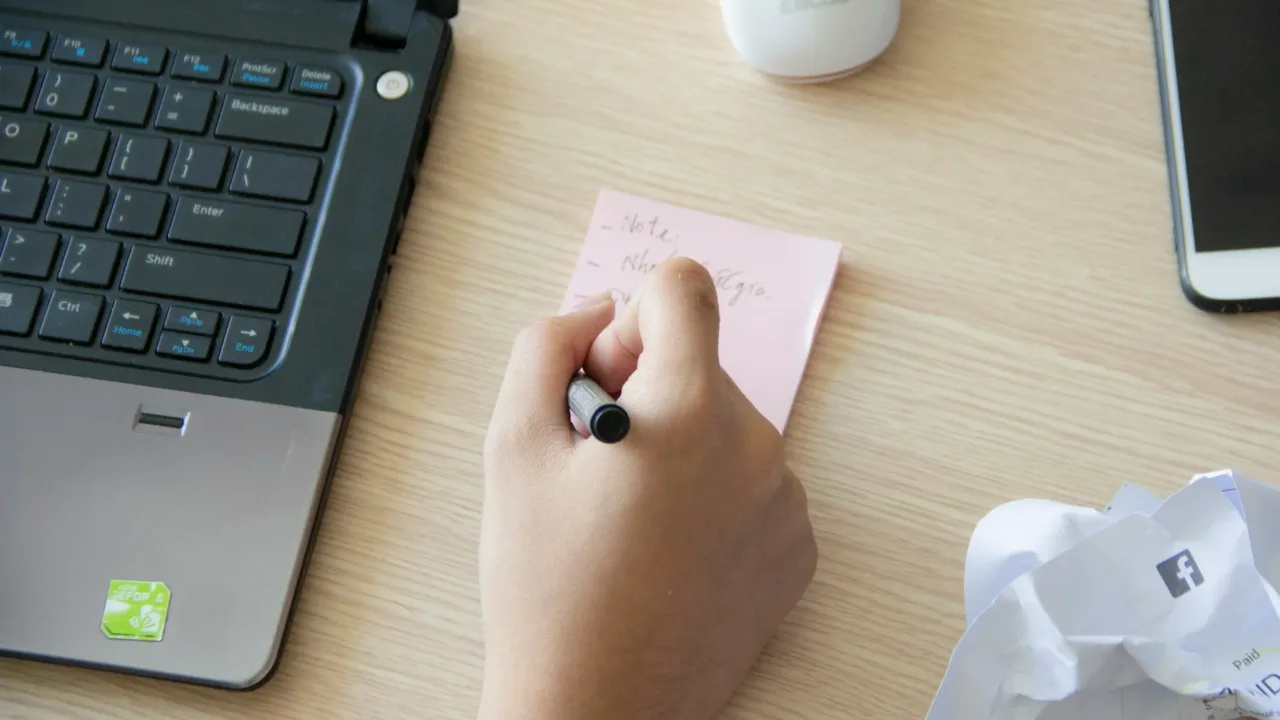 Personne écrivant sur une note adhésive à côté d’un ordinateur portable
